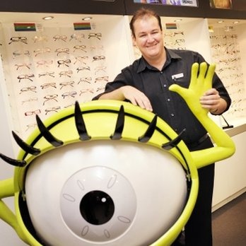 Greg Luke smiling alongside a giant eye display at his Coffs Harbour practice